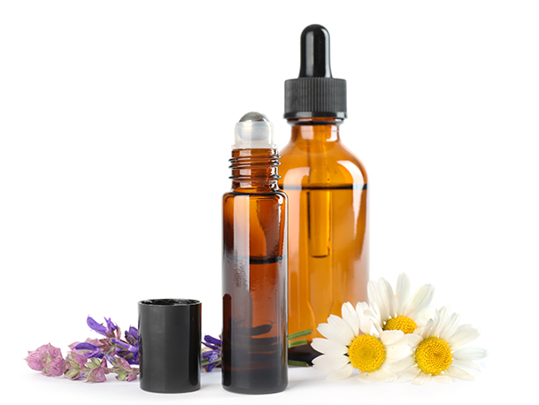 Essential oil dropper bottle and roller bottle beside Lavender and Chamomile flowers