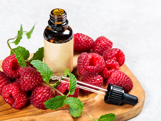 Raspberry Seed Oil in gold bottle surrounded by a handful of raspberries and mint